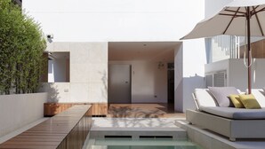 Et moderne poolområde med træterrasse, lounges med puder og et glasindhegnet område.