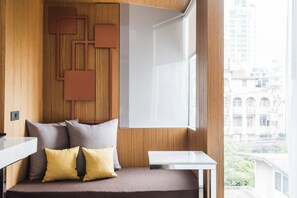 Una habitación moderna con un panel de pared de madera, un sofá con cojines, una mesita y una ventana con vistas a la ciudad.