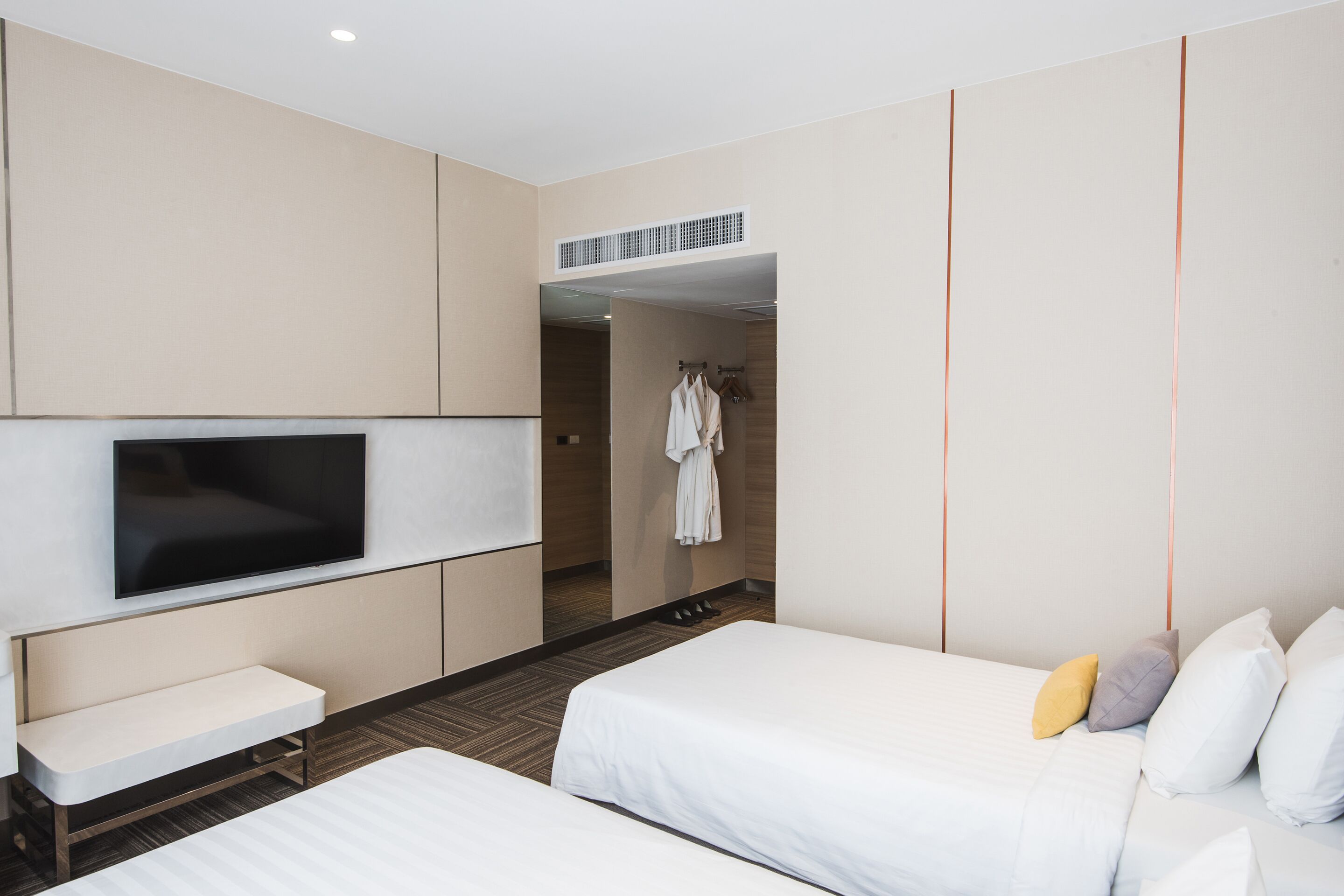 Une chambre d’hôtel avec deux lits, une télévision, un banc et un porte-peignoir.