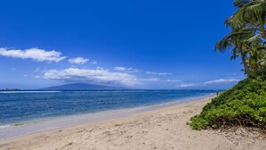 Une plage à l’eau d’un bleu cristallin, bordée d’un rivage sablonneux, avec une montagne qui se profile à l’horizon.