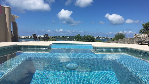 Una piscina con agua azul cristalina, rodeada por un muro de piedra y vista al océano.
