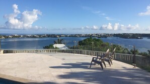 Vista de una zona costera con cielo despejado, agua y una explanada pavimentada con sillas.