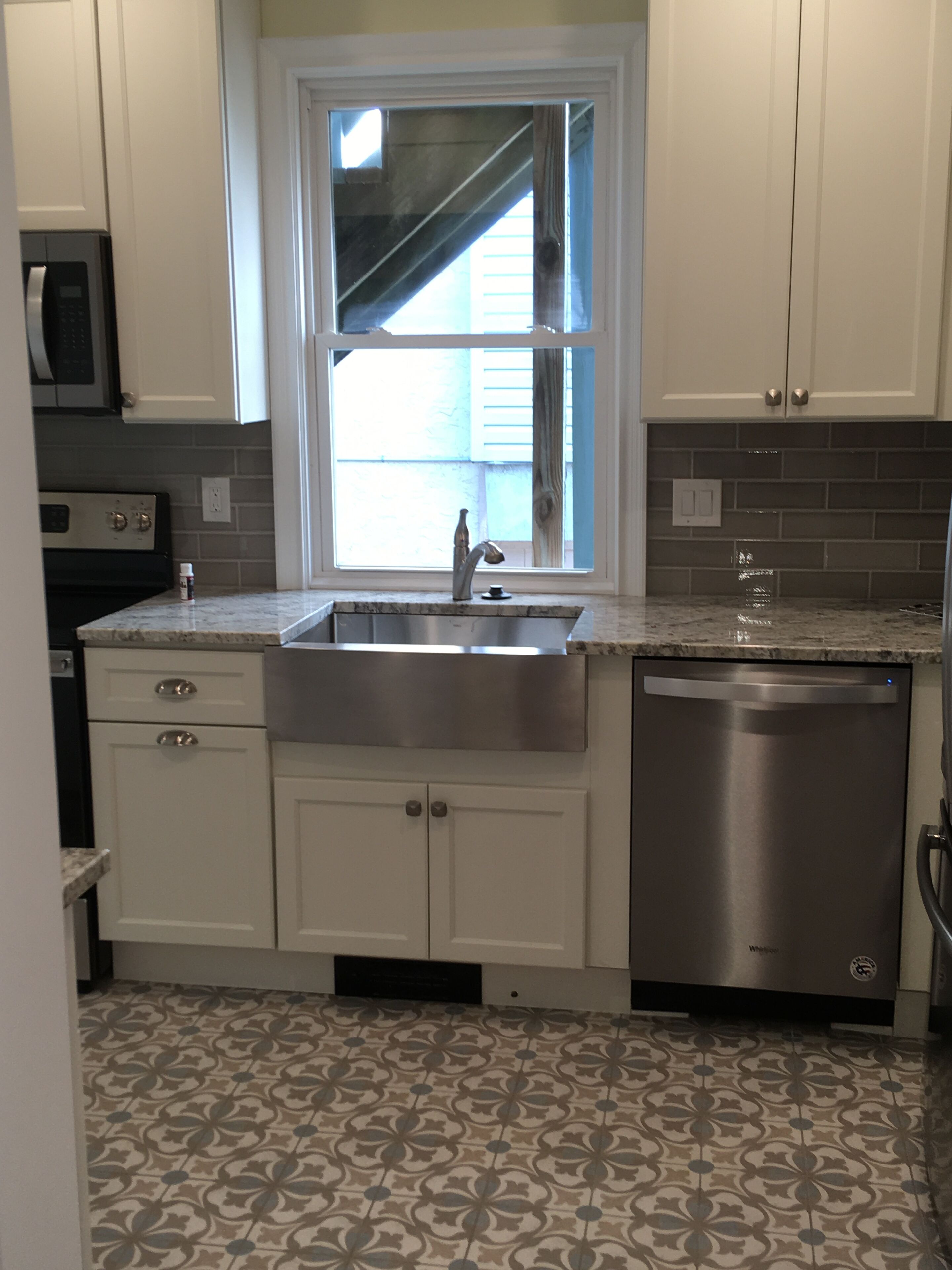 A kitchen with white cabinets, a stainless steel sink, a dishwasher, and a patterned tile floor.