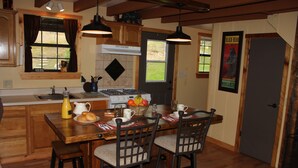 A wooden kitchen with a dining table, chairs, and a stove. There is a window with curtains, a sink, and a door with a poster. - The Ole Bear Rustic Mountain Cabin (Tellico Plains)