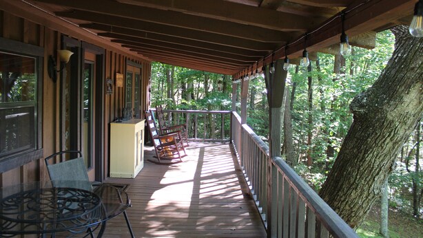 A wooden deck with a glass table and chairs, overlooking a forested area. - The Ole Bear Rustic Mountain Cabin (Tellico Plains)