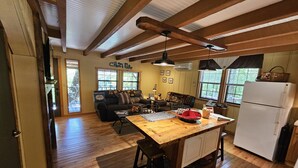 A spacious living area with a wooden floor, a sofa, a coffee table, and a kitchen area with a refrigerator and a dining table. - The Ole Bear Rustic Mountain Cabin (Tellico Plains)