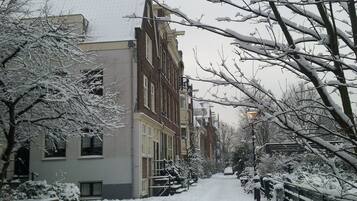 Une rue enneigée bordée d’immeubles à plusieurs étages, avec un étroit chemin piétonnier et des voitures garées.