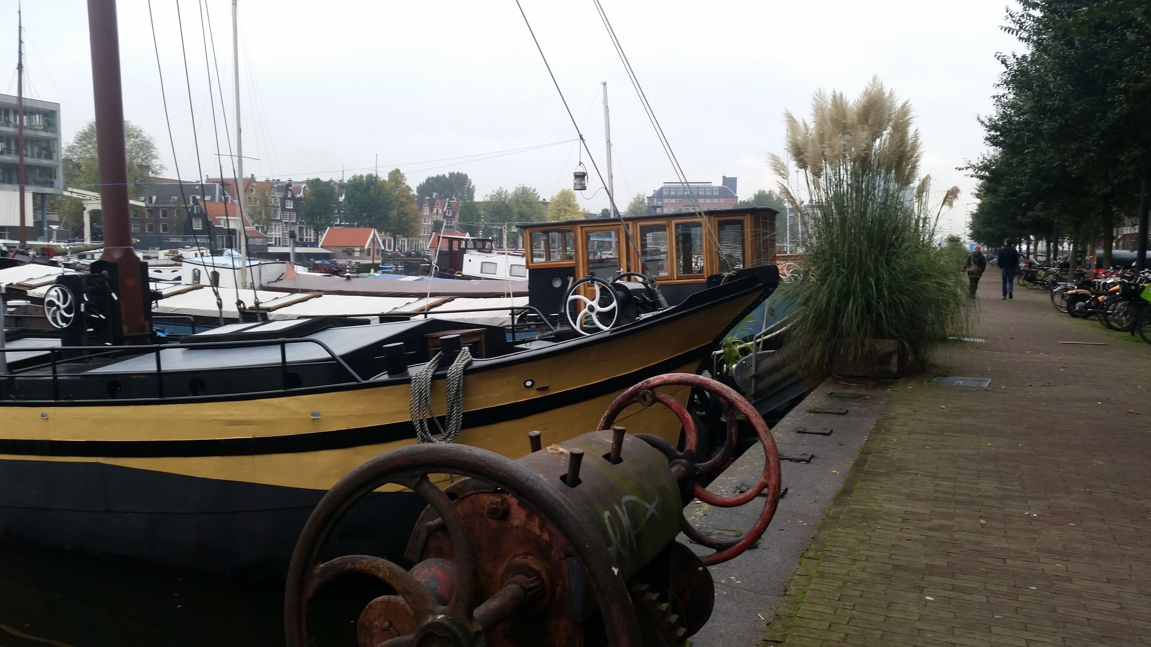 Een historische boot afgemeerd in een jachthaven, met een houten kajuit en een stuurwiel.