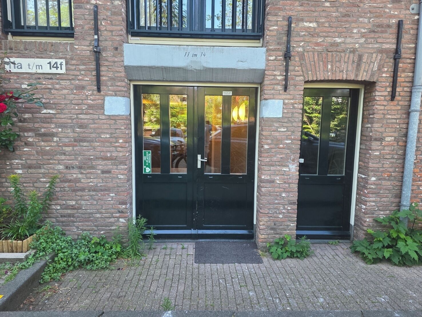 A brick building with two black doors, a small window, and a sign indicating '11 am 14f'.
