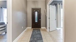 A hallway with a dark wooden door, a patterned rug, and a light-colored tiled floor.