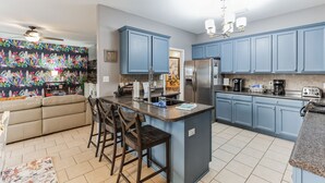 A modern kitchen with blue cabinets, a central island with bar stools, a refrigerator, and a coffee maker.