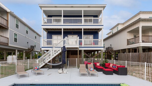 A two-story building with a swimming pool, outdoor seating, and a wooden deck.