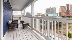 A covered balcony with outdoor furniture, a view of surrounding buildings, and a swimming pool.