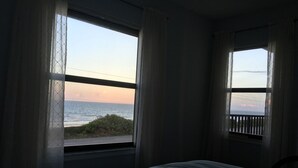 Un dormitorio con un ventanal que ofrece vista al océano y al atardecer.