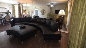 A modern living room with a sectional sofa, a dining area with a table and chairs, and a kitchen in the background. - BEACHFRONT GRAND PANAMA, 1st FLR DIRECT TO BEACH, PET-FRIENDLY. NEXT TO TIKI BAR (Panama City Beach)