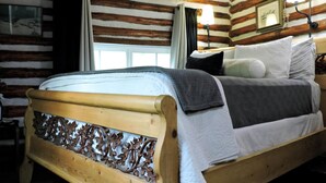 A wooden bed with a decorative headboard in a log cabin-style room with a window and a wall-mounted lamp. - Cabin (Prescott)