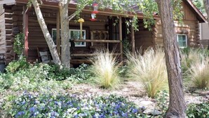 A rustic log cabin with a porch, surrounded by a garden with various plants and flowers. - Cabin (Prescott)