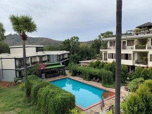 Uma área de piscina com um edifício que possui várias varandas e um restaurante chamado "THE HUT" em primeiro plano.