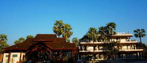 A two-story building with a wooden roof and multiple balconies, surrounded by palm trees.