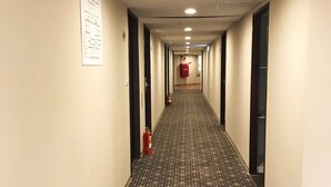 Pasillo de hotel con alfombra estampada, paredes blancas y un extintor a la izquierda.