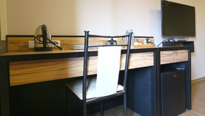 Habitación de hotel con un escritorio de madera, una silla, un televisor y un refrigerador pequeño.