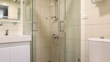 A modern bathroom with a glass-enclosed shower, a white toilet, and a sink with a mirror above it.
