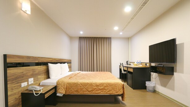 Habitación de hotel con cama, mesita de noche, lámpara y televisor montado en la pared.
