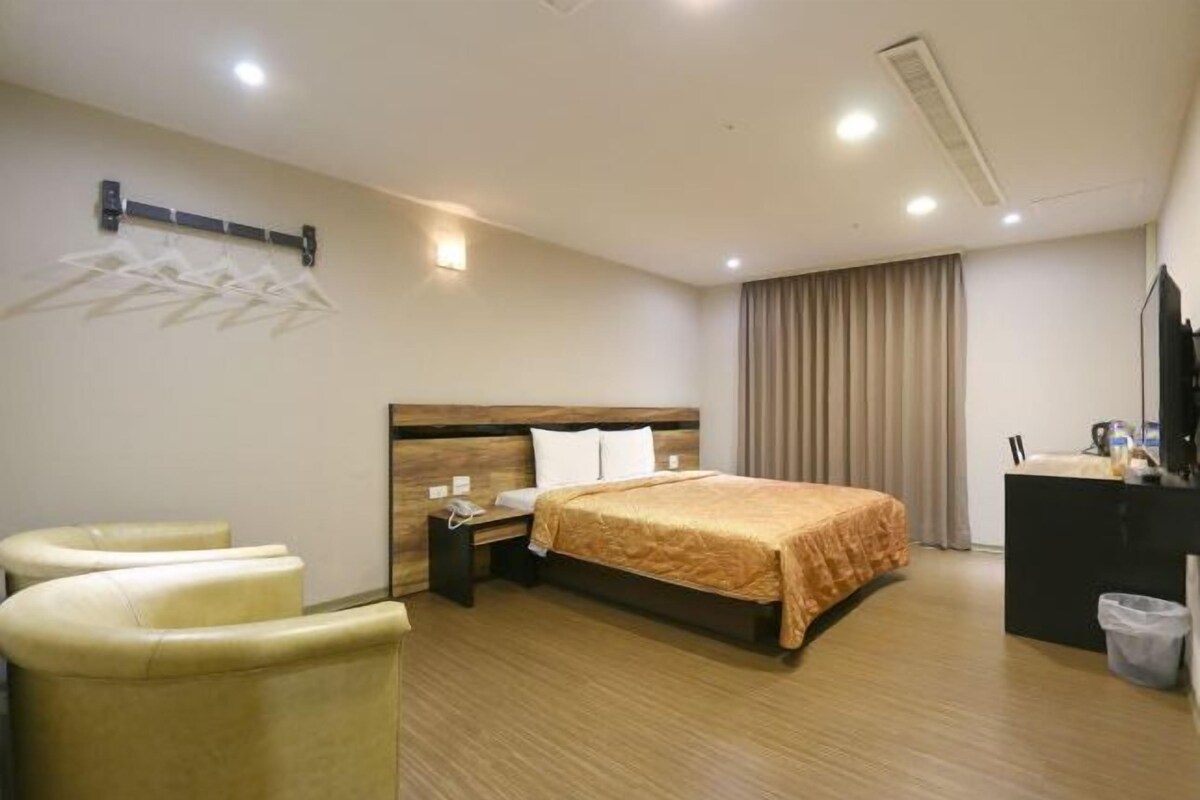 A hotel room with a bed, bedside table, lamp, and a desk with a chair.