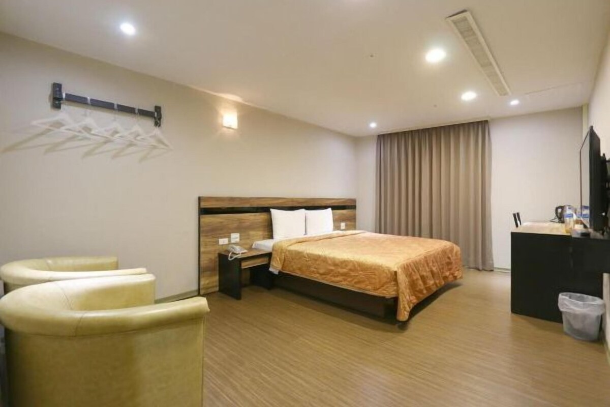 Une chambre d’hôtel équipée d’un lit, d’un bureau, d’une chaise, d’une poubelle et d’un porte-manteau fixé au mur.
