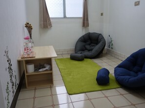 Une pièce avec un tapis vert, une étagère en bois sur laquelle sont posés divers objets, un fauteuil-pouf gris et un fauteuil-pouf bleu.