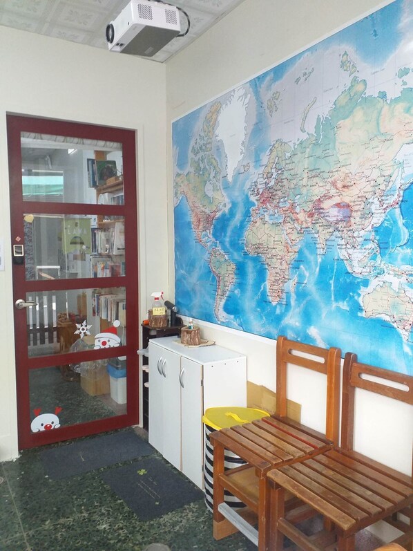 Une pièce avec une grande carte du monde accrochée au mur, un banc en bois, une petite table, un réfrigérateur et une porte dotée d’un panneau en verre.