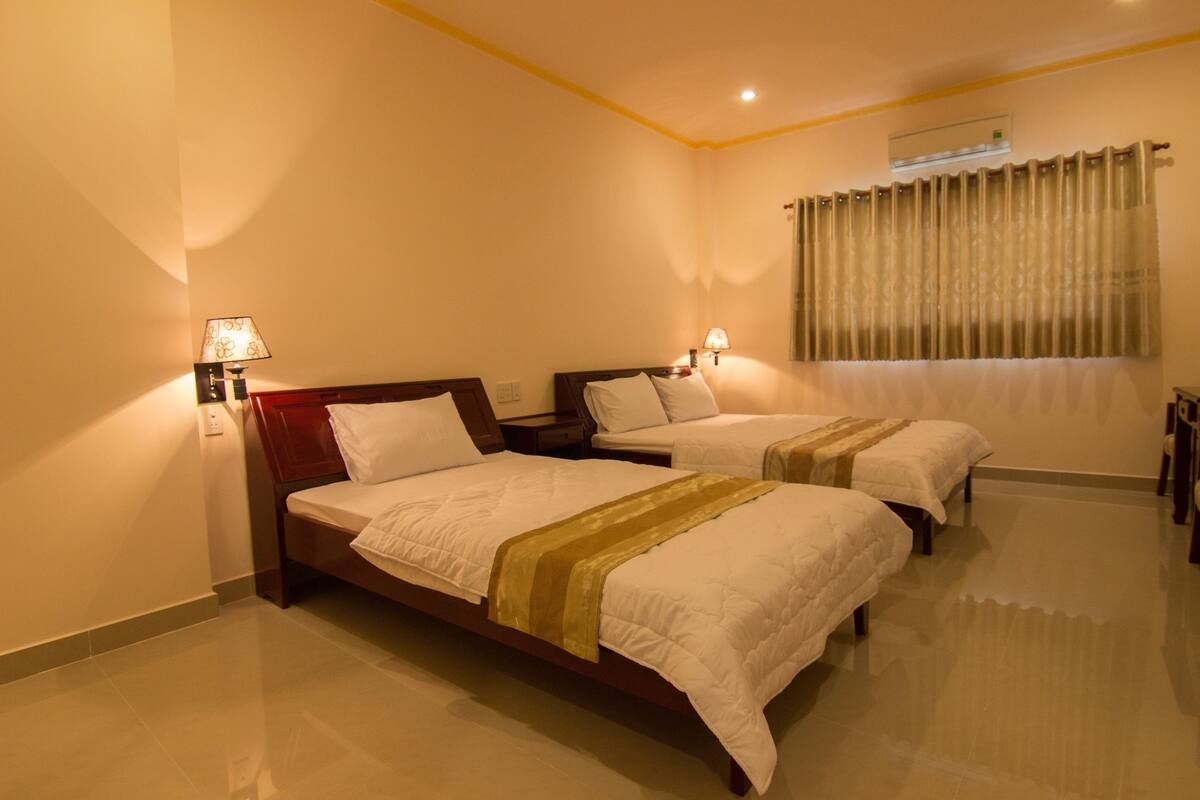 Habitación de hotel con dos camas, cada una con cabecero de madera y ropa de cama blanca. Hay dos lámparas fijadas a la pared a cada lado de las camas.