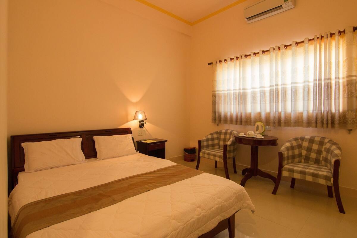 Una habitación de hotel con una cama grande, dos sillas, una mesita y una lámpara.