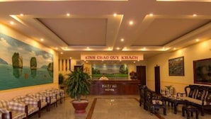 A hotel lobby with a reception desk, check-in counters, seating areas, and a mural of a landscape. - Nhat Ha Hotel (Can Tho)