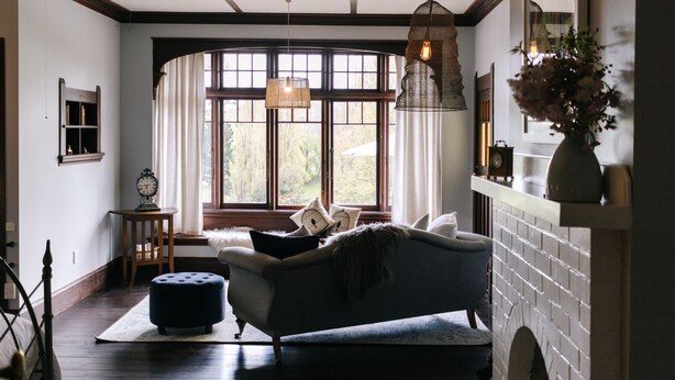 A cozy living room with a sofa, ottoman, and a large window with curtains. - Wallingford Homestead (Wallingford)