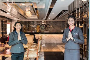 Two individuals in a lobby with marble flooring, elegant furniture, and a chandelier.