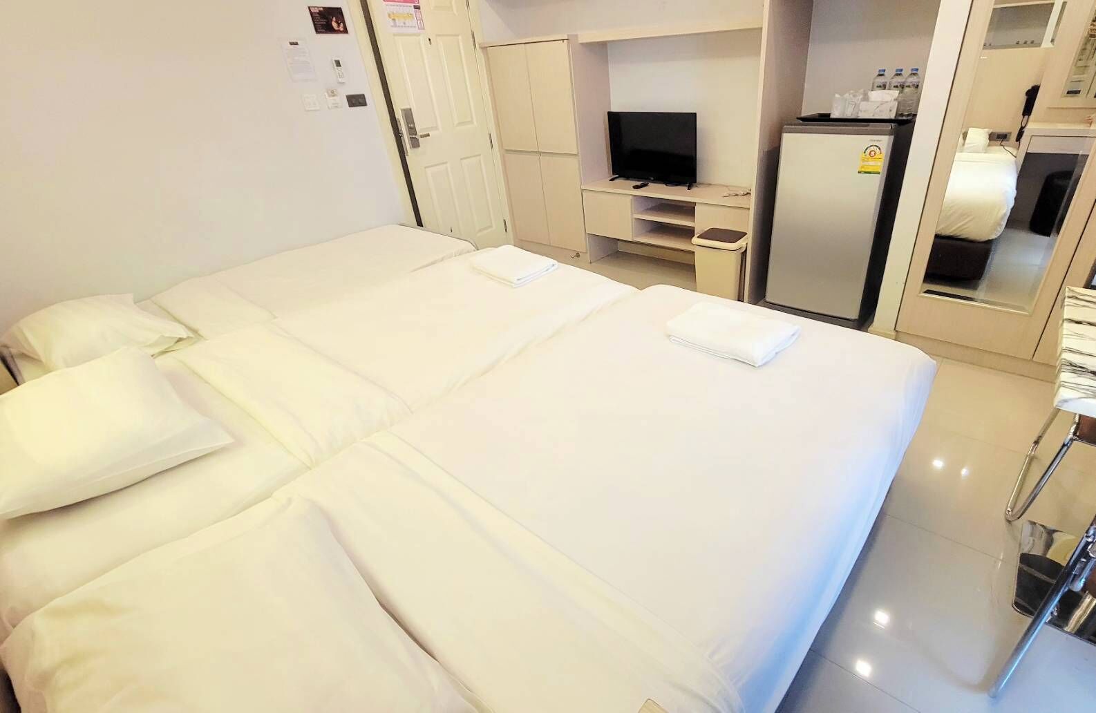 A hotel room with a large bed, a television, a refrigerator, and a small desk area.