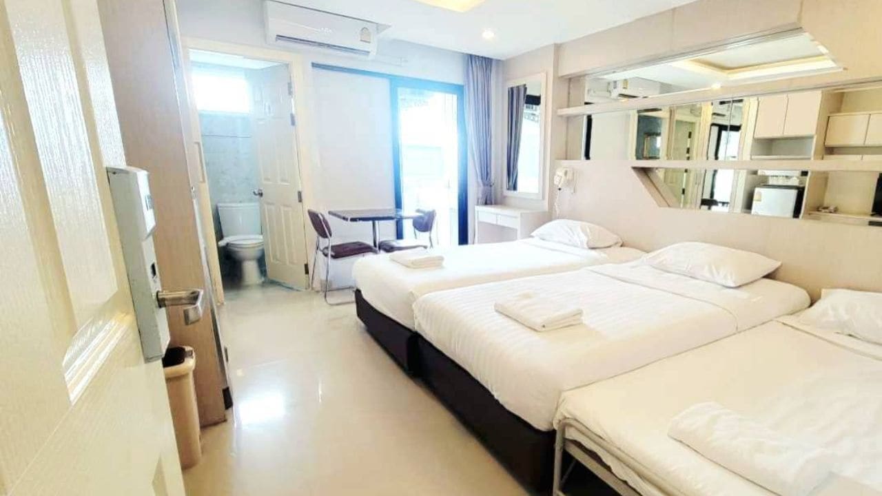 Habitación de hotel con dos camas, un escritorio, una silla y un baño visible a través de una puerta abierta.