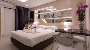 Una habitación de hotel moderna con una cama grande, un escritorio con una silla, un espejo y un florero con flores.