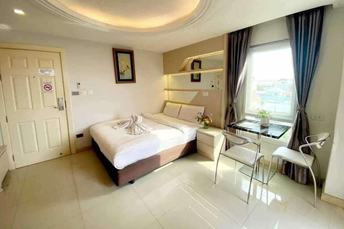 A hotel room with a bed, a desk, a chair, a window with curtains, a door, and a ceiling with recessed lighting.