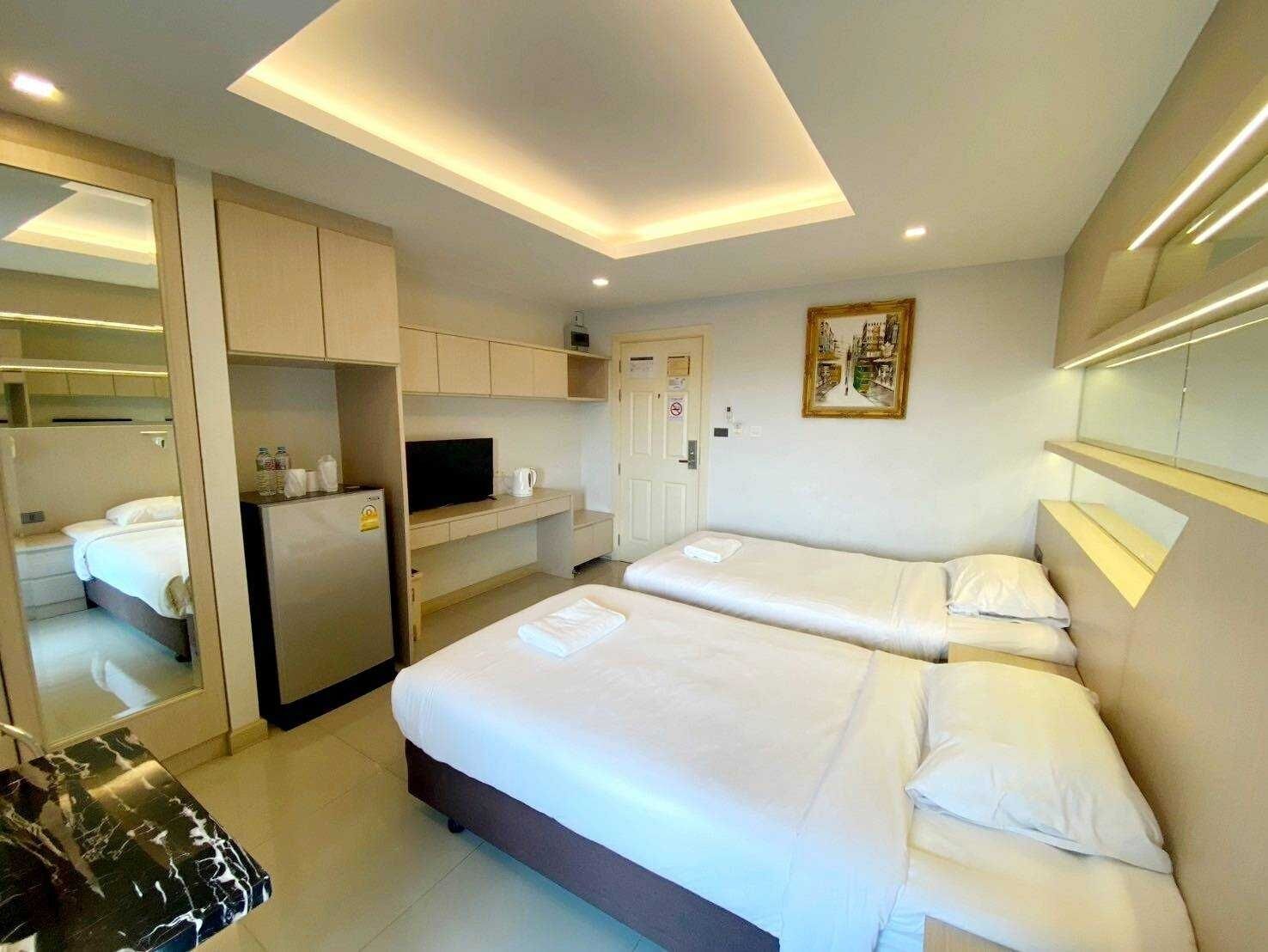 A modern hotel room with two beds, a kitchenette, a television, and a painting on the wall.