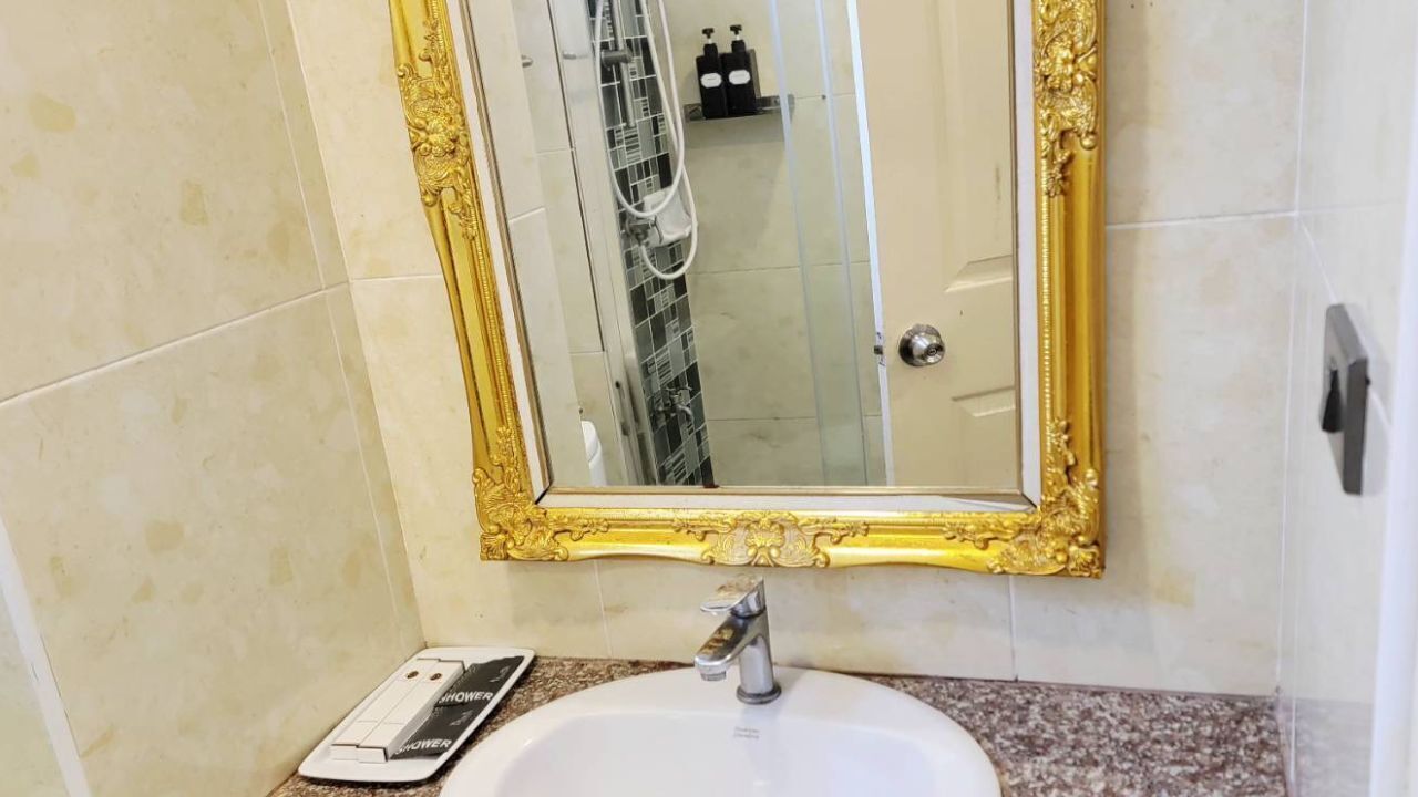 Un baño con un lavabo blanco, un espejo con marco dorado y una zona de ducha visible al fondo.