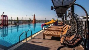 Zona de piscina con tobogán, terraza de madera y una silla colgante.