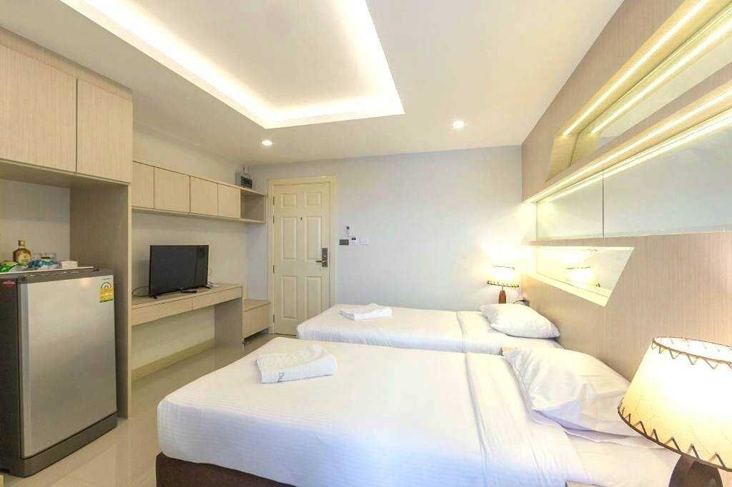 Ein Hotelzimmer mit zwei Betten, einem Fernseher auf einem Regal, einem Kühlschrank und einem beleuchteten Spiegel.