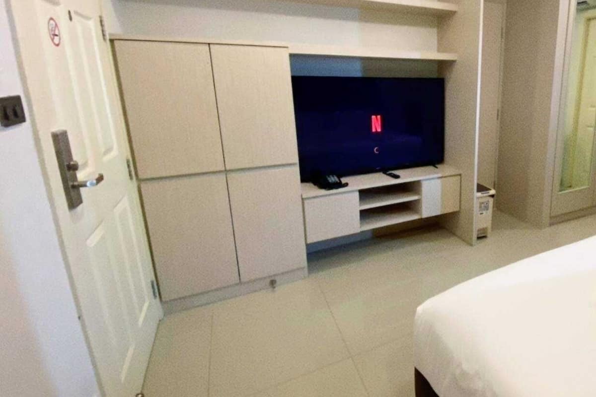 A hotel room with a large flat-screen TV on a white entertainment unit, a bed with white bedding, and a door with a 'No Entry' sign.