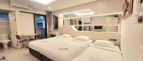 A modern hotel room with two beds, a small desk, and a bathroom.