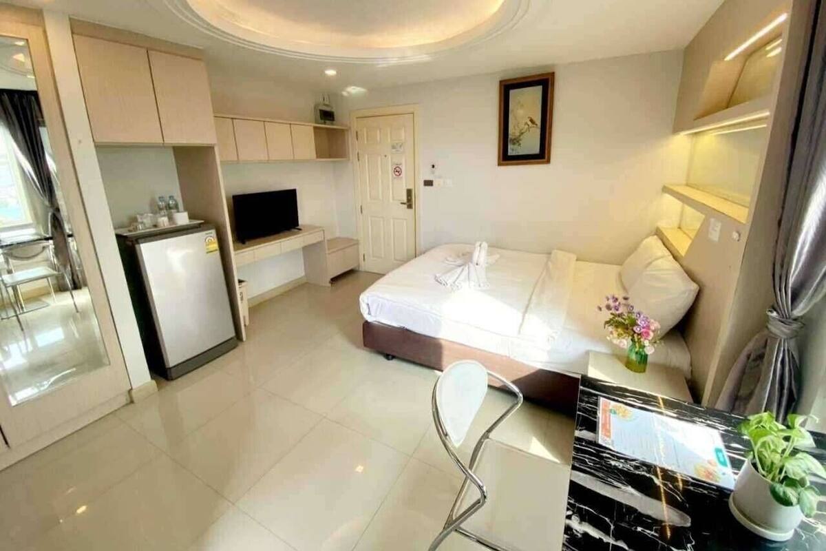 A modern hotel room with a bed, a desk, a chair, a small kitchenette, and a bathroom.