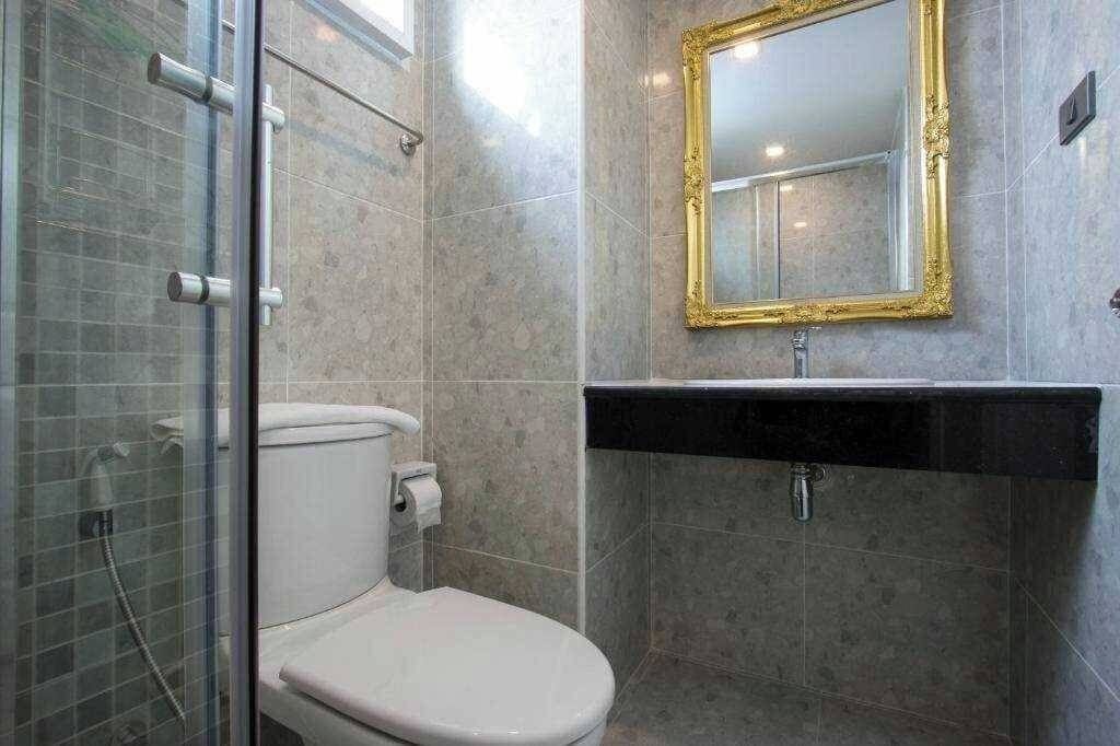 Un baño con cabina de ducha de vidrio, inodoro blanco y lavamanos negro con espejo de marco dorado.