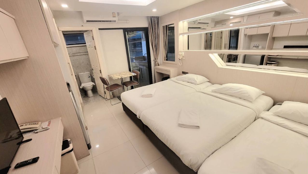 A hotel room with a large bed, a desk with a chair, a small table, and a bathroom visible through an open door.
