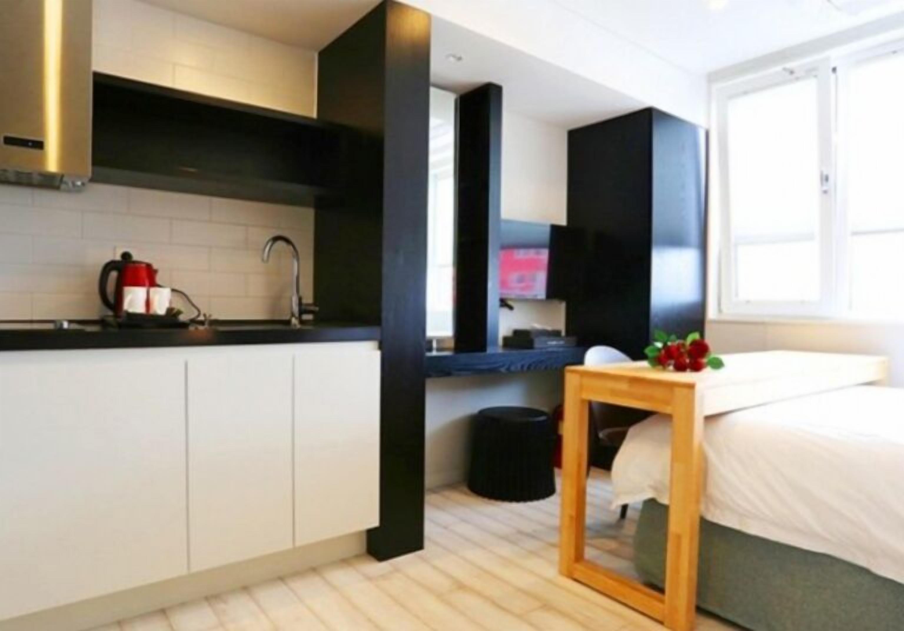 Una cocina moderna con armarios blancos, encimera negra y una mesa de madera con un jarrón de flores.